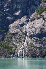 Waterfall Flowing Down Rocky Cliff into Turquoise Glacier Water