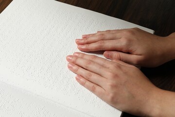 Blind woman reading book written in Braille at wooden table, closeup