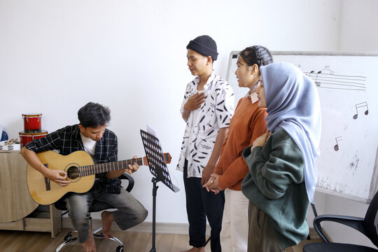 Happy Asian High School Students Learning Playing Musical Instrument And Singing In Class	