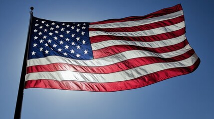 Obraz premium A large American flag waves in the wind against a bright blue sky with white clouds,