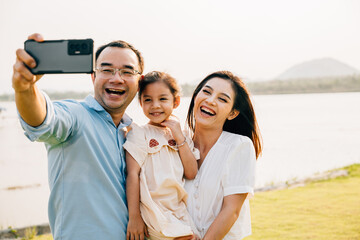 Asian family taking selfie picture with smartphone outdoor nature park, Happy smile father mother...