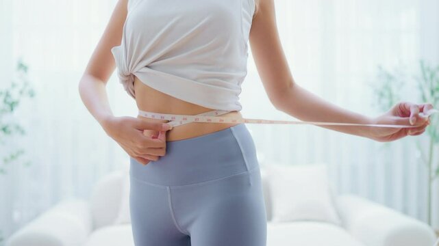 Young Asian woman in sportswear measuring her waist with a tape. Diet and healthy concept. Body shape slim