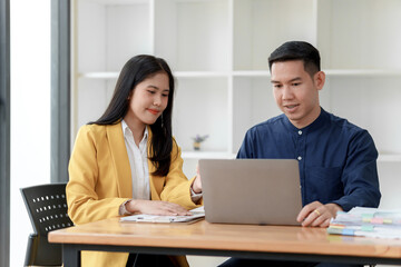 A professional setting with two individuals collaborating over a laptop, showcasing teamwork and...