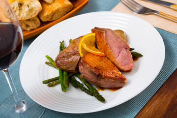Juicy roasted duck breast served with baked onions, pickled asparagus and slice of orange..