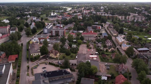A drone captures an aerial view of the small town of Valka, showcasing its buildings, streets, and surrounding greenery. The peaceful townscape contrasts with the natural beauty of the area.