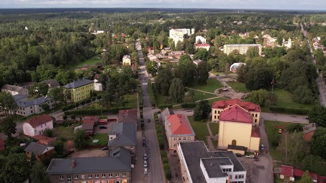 A drone captures an aerial view of the small town of Valka, showcasing its buildings, streets, and surrounding greenery. The peaceful townscape contrasts with the natural beauty of the area.