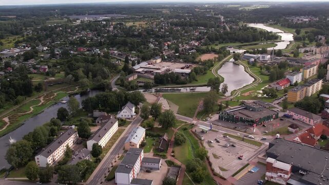 A drone captures an aerial view of the small town of Valka, showcasing its buildings, streets, and surrounding greenery. The peaceful townscape contrasts with the natural beauty of the area.