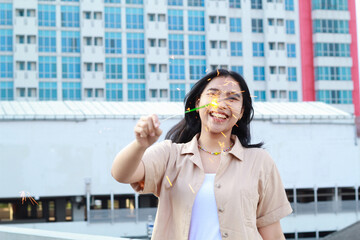 Fototapeta premium happy asian young woman holding sparklers celebrate new year eve in outdoor roof top with city building background