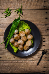 Pork-filled sago in a black plate with long leaf coriander and lettuce on an old wooden table with green chilli peppers on a wooden table