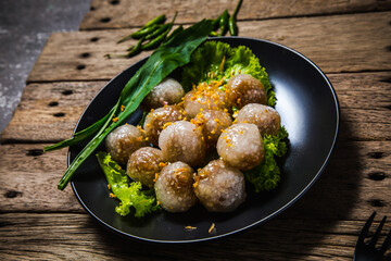 Pork-filled sago in a black plate with long leaf coriander and lettuce on an old wooden table with green chilli peppers on a wooden table