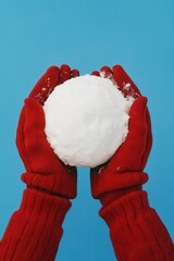 Hands holding a snowball against a bright blue background.