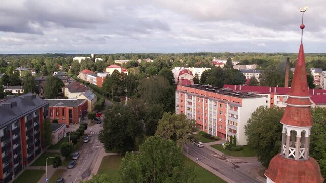 A drone captures an aerial view of the small town of Valka, showcasing its buildings, streets, and surrounding greenery. The peaceful townscape contrasts with the natural beauty of the area.