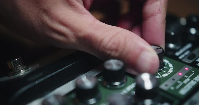 Amazing slow motion shot of a young musician using his hands to move the knobs on a Boss Re-202 Space Echo delay pedal for his guitar in a live show and recording songs in a studio.