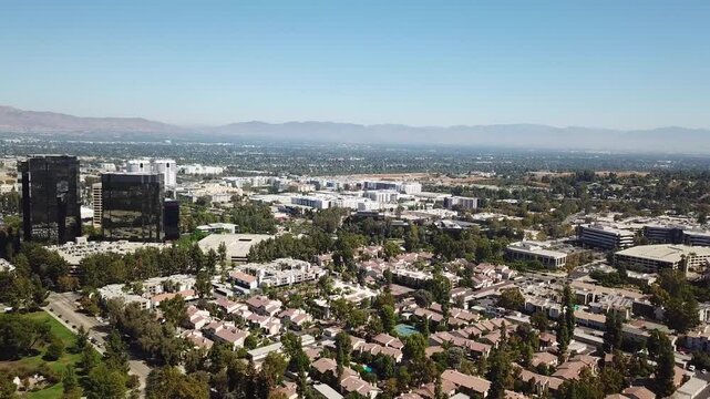 American housing area of Woodland Hills, Los Angeles during sunny autumn day. Modern mirrored AIG Capital Service Building. Silhouette of mountain Formation in backdrop.Slow aerial forward wide shot.
