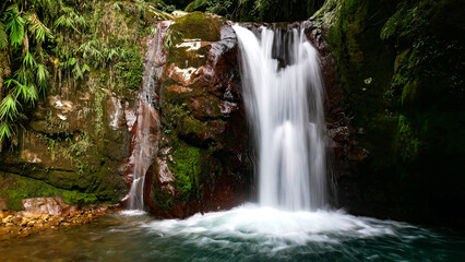 Obraz premium Gleweran is the name of this small waterfall, flowing from a cliff covered in green moss, with large rocks and tropical trees around it. Located in Mount Halimun Salak National Park, Bogor, Indonesia.