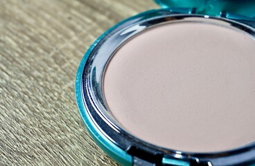 Compact powder light shade make up in round box container isolated on horizontal ratio brown wooden table surface background.