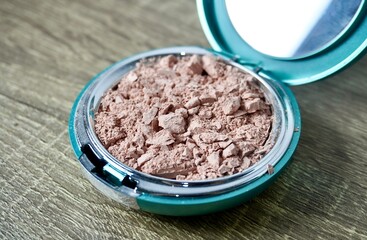 Crushed destroyed compact powder in round box container isolated on horizontal ratio brown wooden...