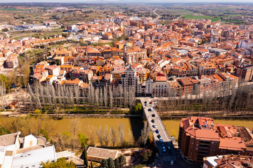 Picturesque aerial view of Spanish city of Aranda de Duero with terracotta tiled roofs of residential buildings on banks of river in spring