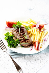 Grilled Steak with french fries and fresh tomatoes. White wooden background.