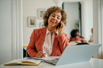 Obraz premium Successful businesswoman in modern office talking on the phone and working on a laptop