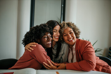Obraz premium Embraced small group of business women hugging each other and smiling during a business meeting