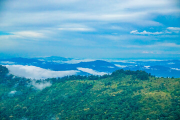 Obraz premium A breathtaking view of lush green mountains with misty clouds hovering over the landscape and distant hills.