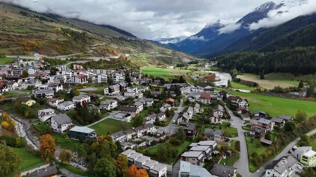 Aerial flyover Scoul Town in Switzerland with houses and apartment blocks. Swiss Community between mountains and cloudscape. Sunny fall season day in Switzerland. Wide shot.