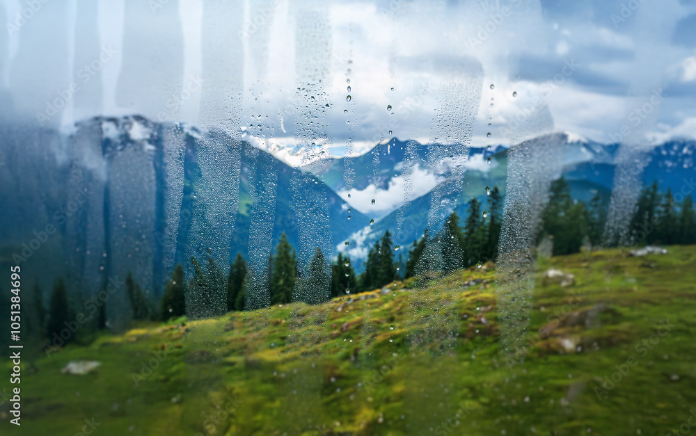 Poster A view of a mountainous landscape through a rain-streaked window, with clouds obscuring the peaks and droplets of water clinging to the glass.