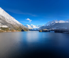 Obraz premium A tranquil mountain lake with snow capped peaks reflected in the calm blue water under a bright blue sky.