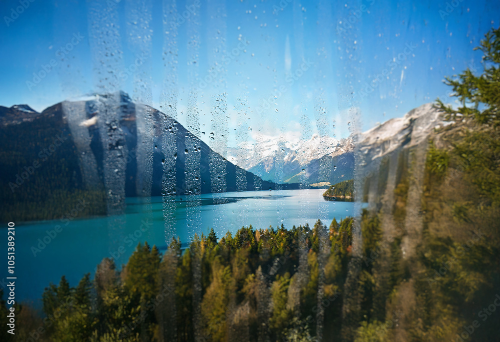 Poster a view of a lake surrounded by mountains seen through a window with water droplets.