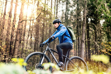 Obraz premium Active man on bike in the middle of beautiful forest, early autumn morning. Concept of healthy lifestyle. Low angle view.