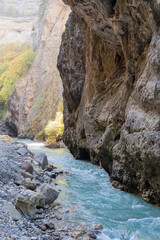 Obraz premium Stormy mountain river Chegem flows in deep crevice along bottom of Chegem Gorge. Steep cliffs hang over river with emerald transparent water. In depths of gorge, semi-darkness reigns.