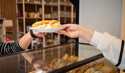 close-up of hands receiving a plate of tapas over the food counter, in a restaurant. 