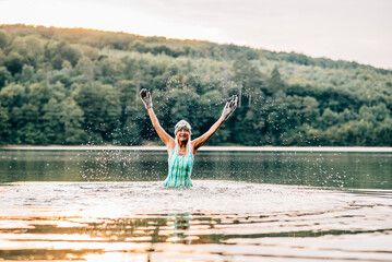 Cold water swimming for elderly women. Senior sporty women standing in lake during cold evening, arms in the air.