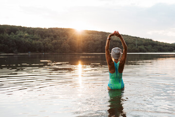 Cold water swimming for elderly women. Rear view of sporty women standing in lake during cold...