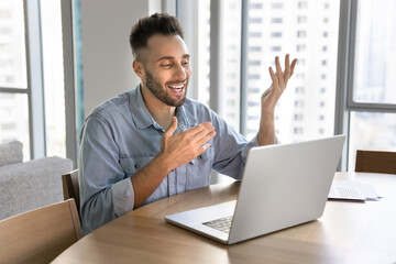 Fototapeta premium Happy Latin vlogger man broadcasting online on social media, talking on video chat at laptop, speaking with toothy smile, moving hands, using online conference call for work communication