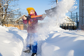child clears path from snow in backyard of house in winter in village with shovel. snow removal