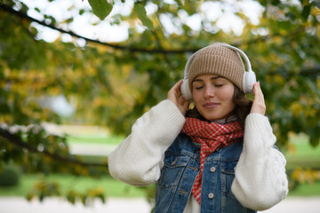 Beautiful young woman on a walk in the autumn park, listening to music and enjoying a peaceful moment for herself.