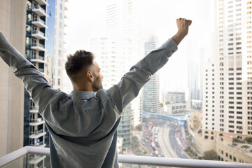 Excited successful homeowner enjoying being in new apartment, standing on balcony of higher floor,...