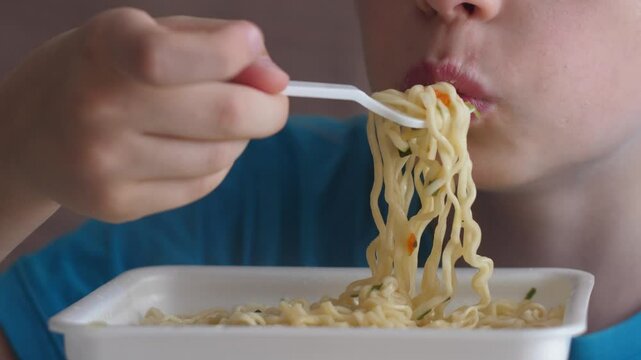 Caucasian boy 10-12 years old eats instant noodle soup, child with appetite vermicelli plastic fork