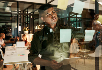 Business, man and tablet with sticky notes in office for brainstorming project ideas and kpi review at night. Professional, employee and digital app by glass wall for progress report and development