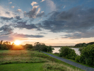 A beautiful sunset by Corrib river with a path next to it. The sky is cloudy and the sun is setting, creating a serene and peaceful atmosphere. Galway city, Ireland. Nature scene.