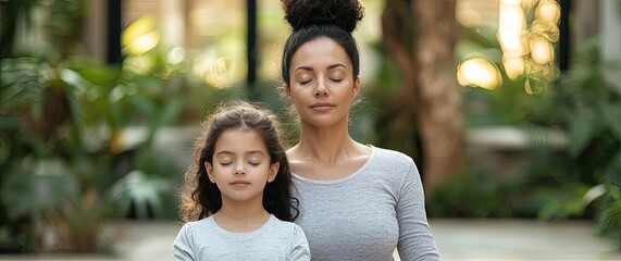 Mom and daughter meditating peacefully in a lush environment.