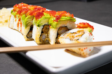 Close up of sushi roll with fried shrimp inside and fresh avocado and salmon on the top