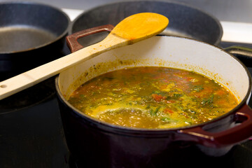 A vegetable stew is boiling in a reddish pot. A wooden spoon rests on one side.