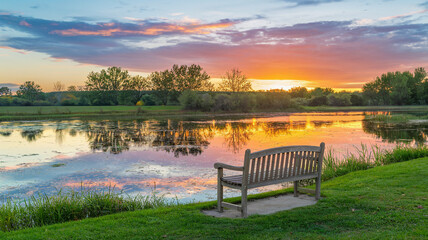 Obraz premium Peaceful Sunset Reflection by the Lake with a Bench