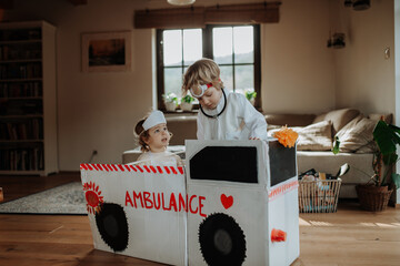 Siblings in doctor uniform is playing hospital. Little ambulance paramedics sitting in cardboard...