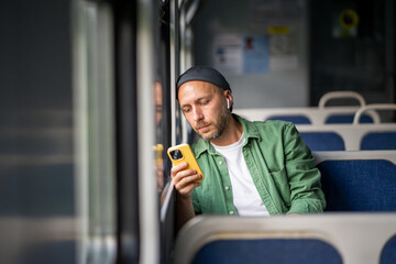 Thoughtful man concentrating on mobile phone rides on electric train reading e-book, scrolling...