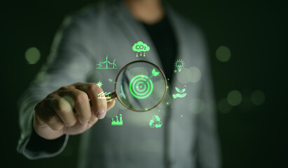 Hand holding a magnifying glass focusing on a target with a leaf, Green Energy and Sustainability...