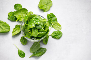 Spinach leaves in a transparent glass bowl on light gray table background. Heap of Baby spinach fresh leaves close up, border design. Healthy vegan food, diet, dieting. Top view
